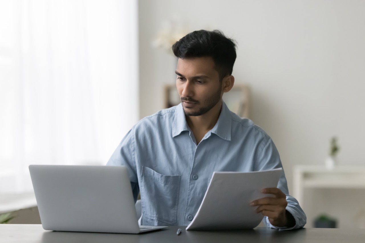 Man looking at his laptop with papers on the other hand